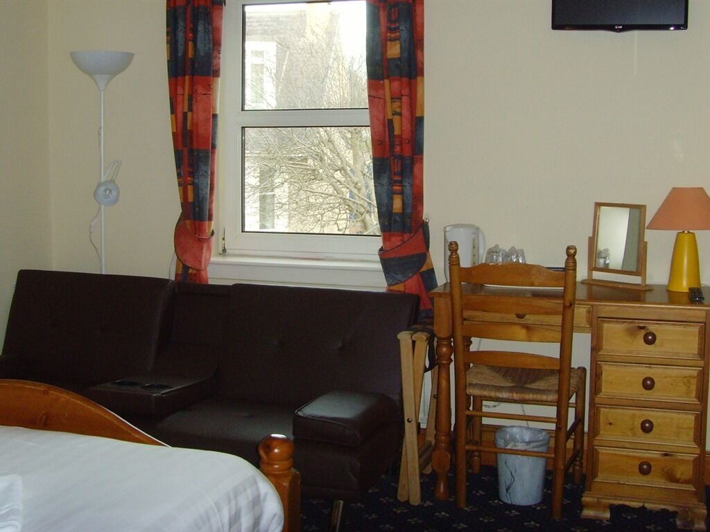 A hotel room with a bed, a dark-colored sofa, a wooden chair, a wooden dresser, a desk, and a television on the wall.