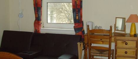 A hotel room with a bed, a dark-colored sofa, a wooden chair, a wooden dresser, a desk, and a television on the wall.