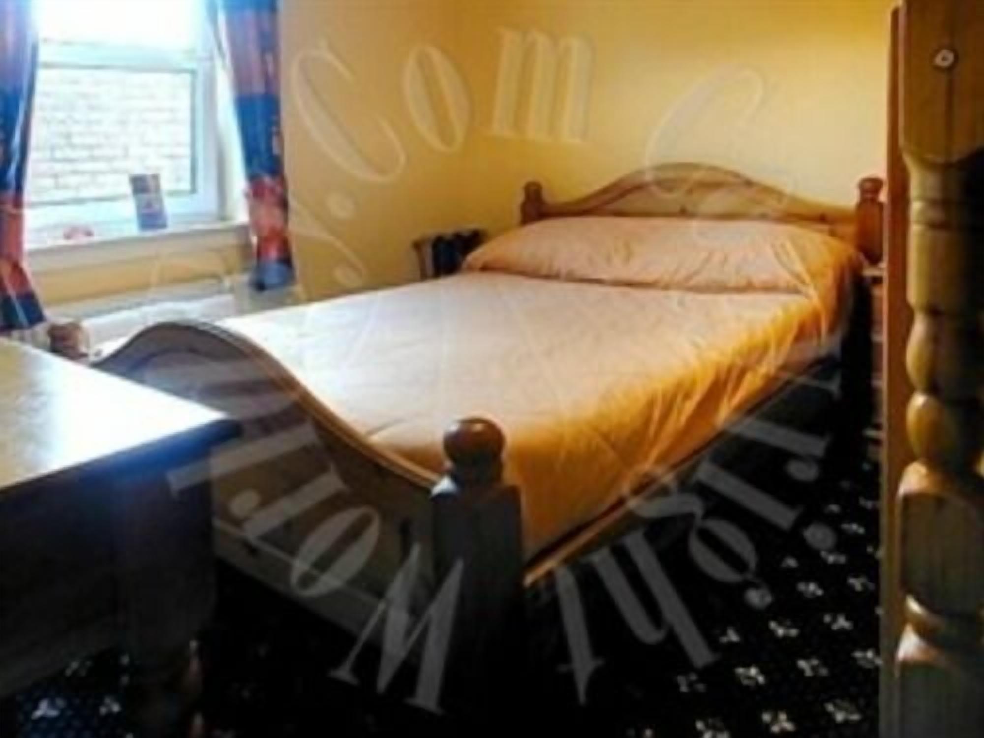 A bedroom with a bed, a wooden headboard, a window with curtains, and a nightstand.