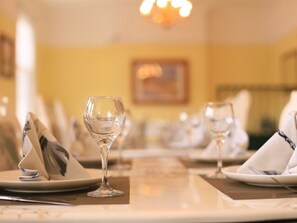 A dining table set with plates, glasses, and napkins, with a chandelier in the background. - Twin Lions Hotel (Edinburgh)