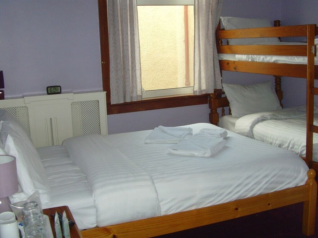 A single bed with a wooden headboard, a bedside table with a lamp, and a window with curtains.