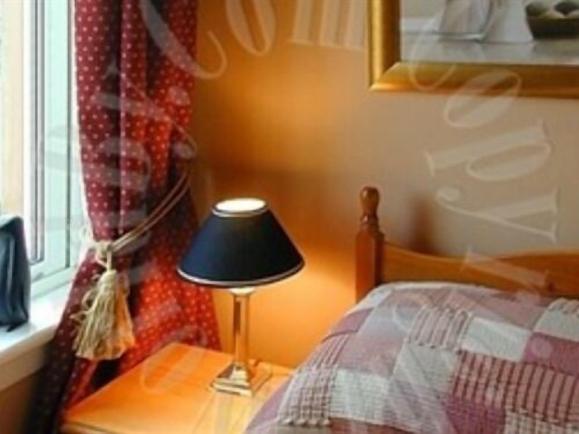 A room with a bed, a nightstand, a lamp, a window with curtains, and a framed picture on the wall.