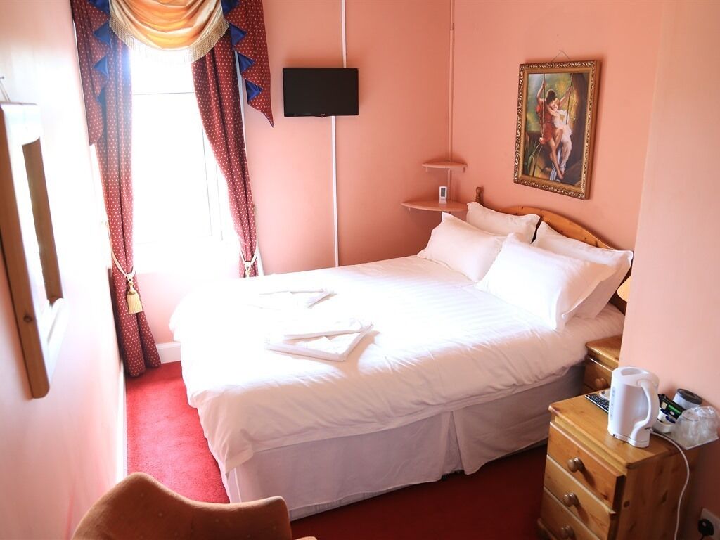 Ein Hotelzimmer mit einem Bett, einem Nachttisch mit Lampe, einem Gemälde an der Wand und einem Fernseher über dem Bett.