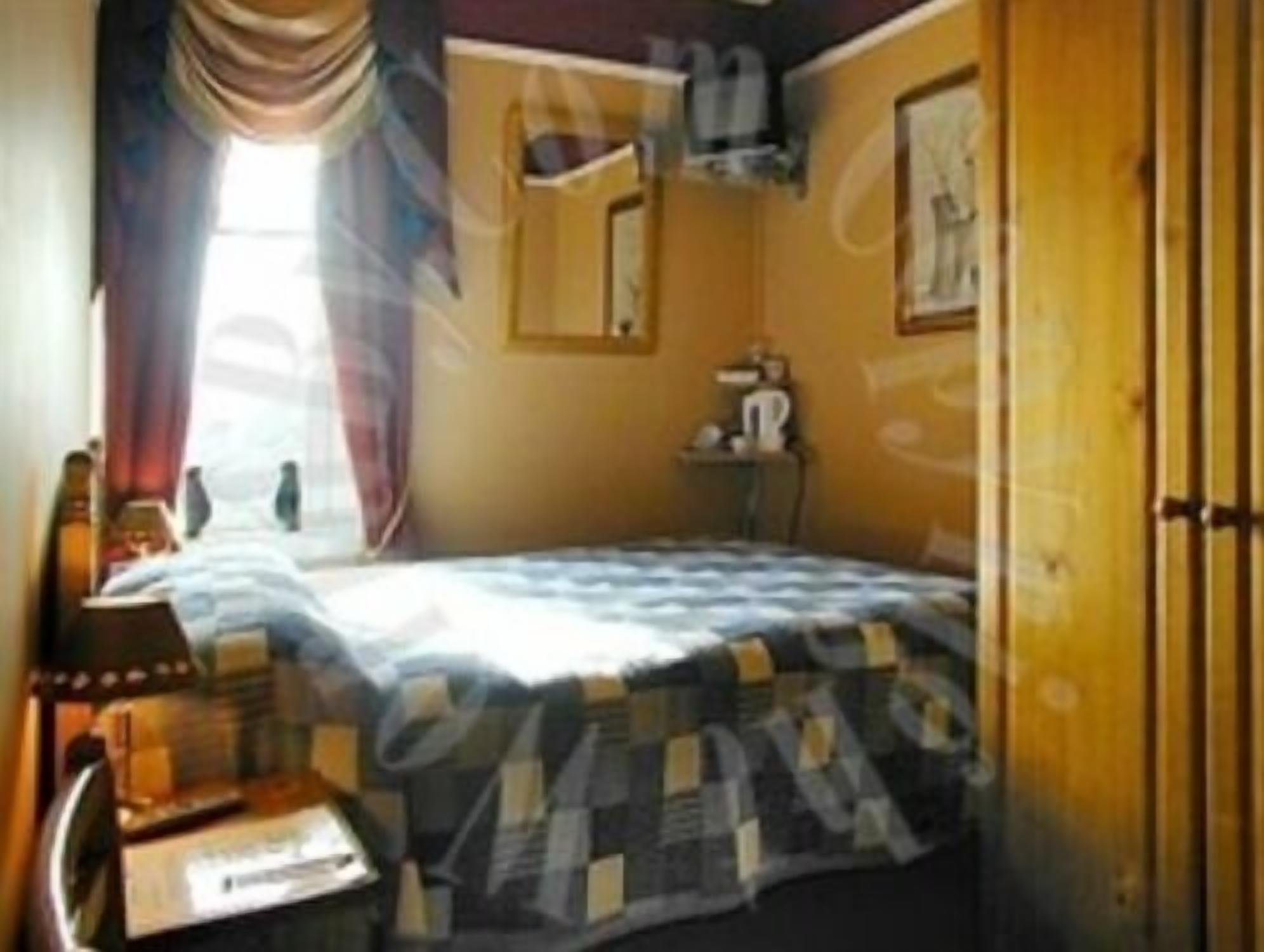 A bedroom with a bed, a nightstand, a lamp, and a window with curtains.
