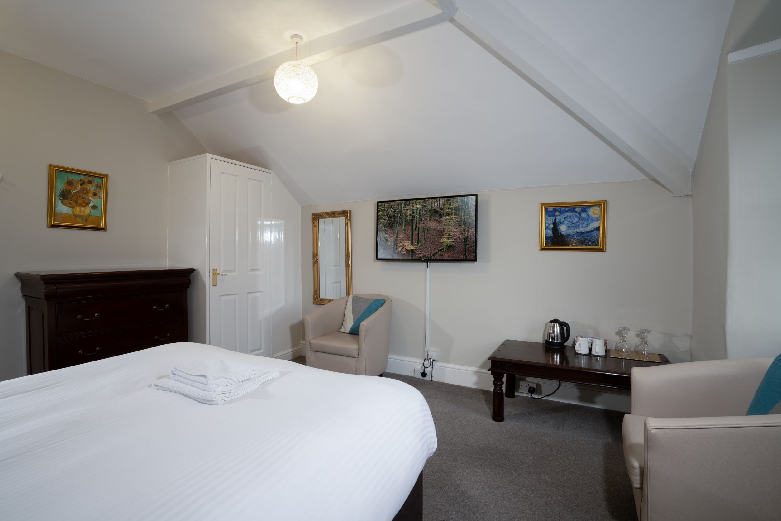 Ein Hotelzimmer mit Bett, Schreibtisch, Stuhl, Kleiderschrank und Bildern an den Wänden.