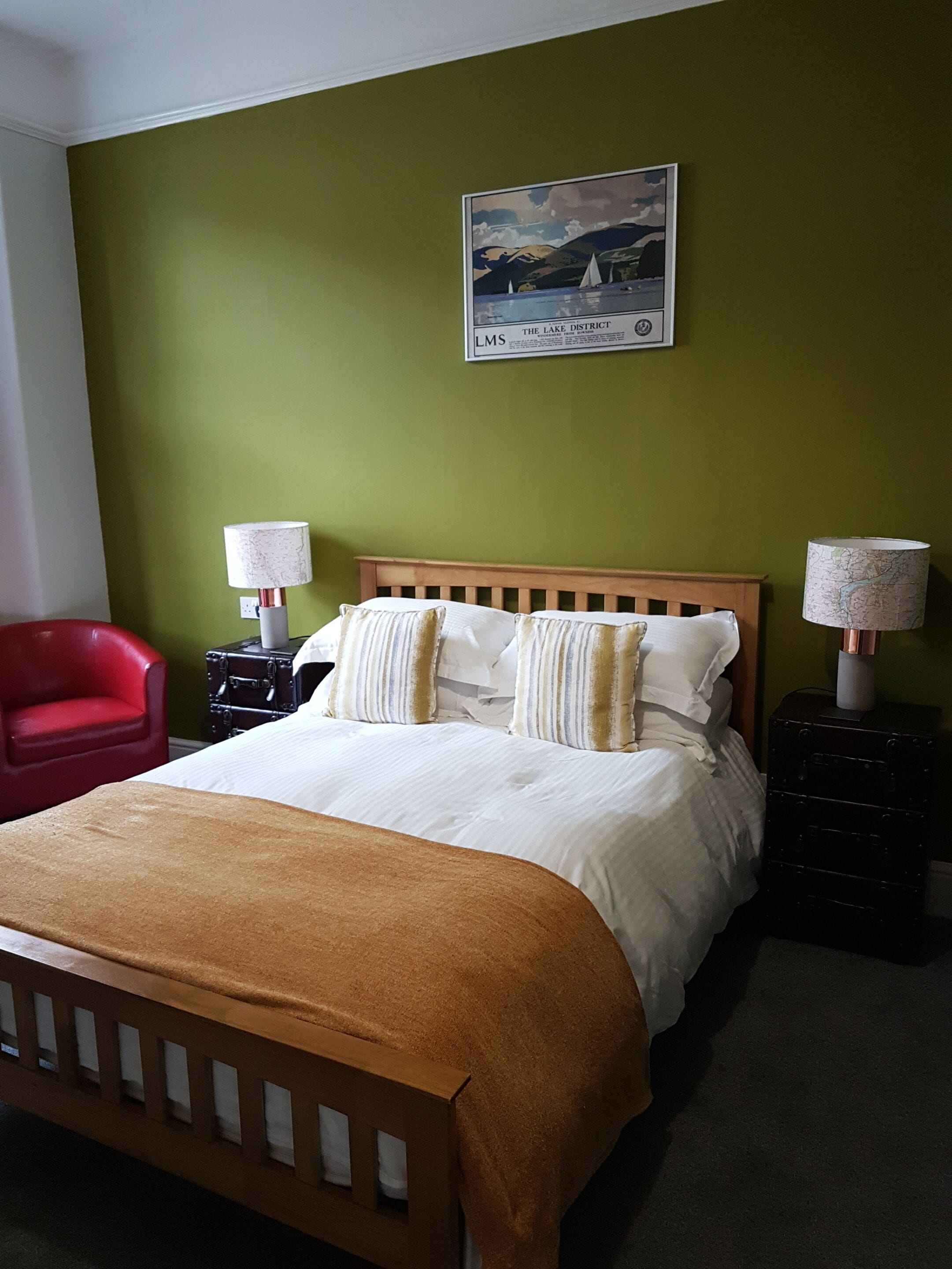 A bedroom with a wooden bed, green walls, a framed picture, two bedside tables with lamps, and a red chair.
