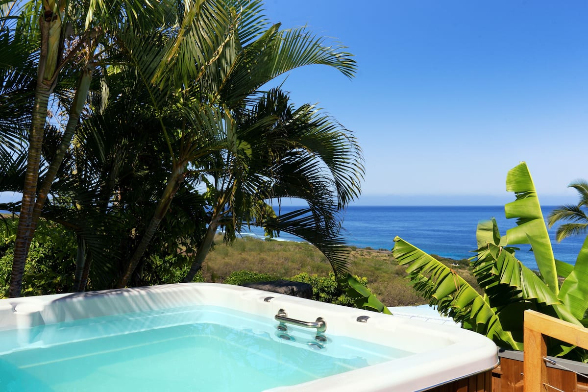 A hot tub with a view of the ocean and tropical vegetation.