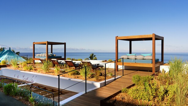 Une terrasse sur le toit avec des sièges en bois, une piscine et une vue sur l’océan.