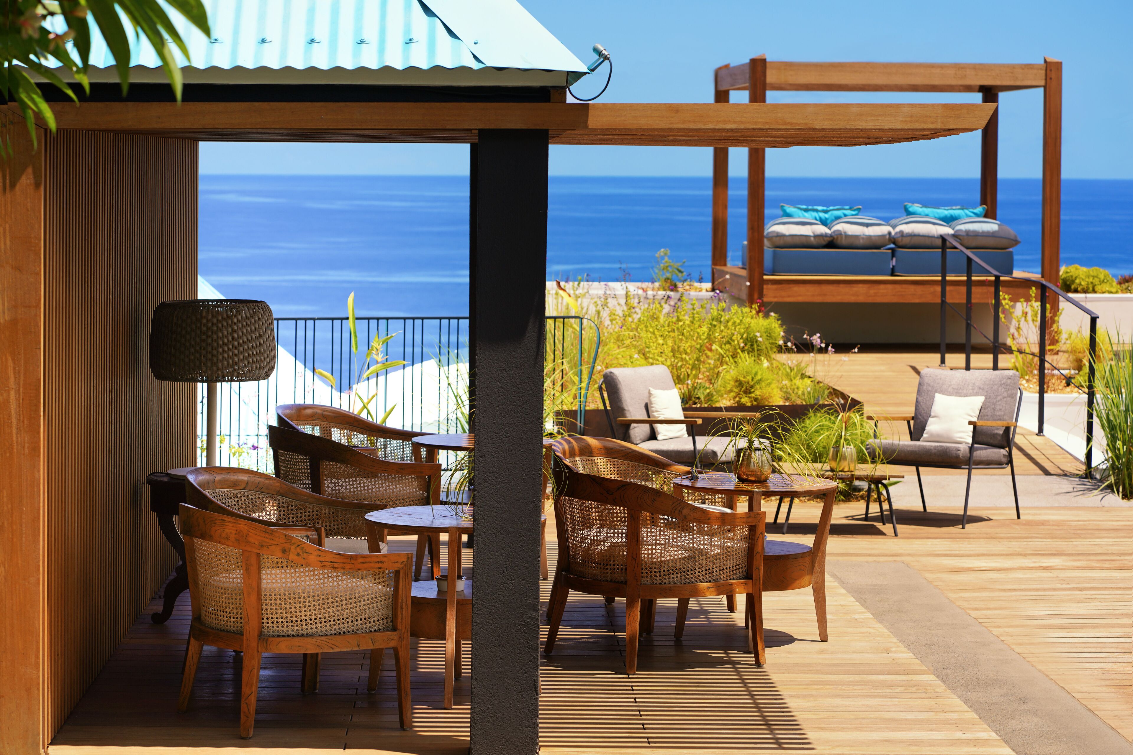 Une terrasse en bois, agrémentée de chaises et de tables en osier, qui offre une vue imprenable sur un océan d’un bleu profond.
