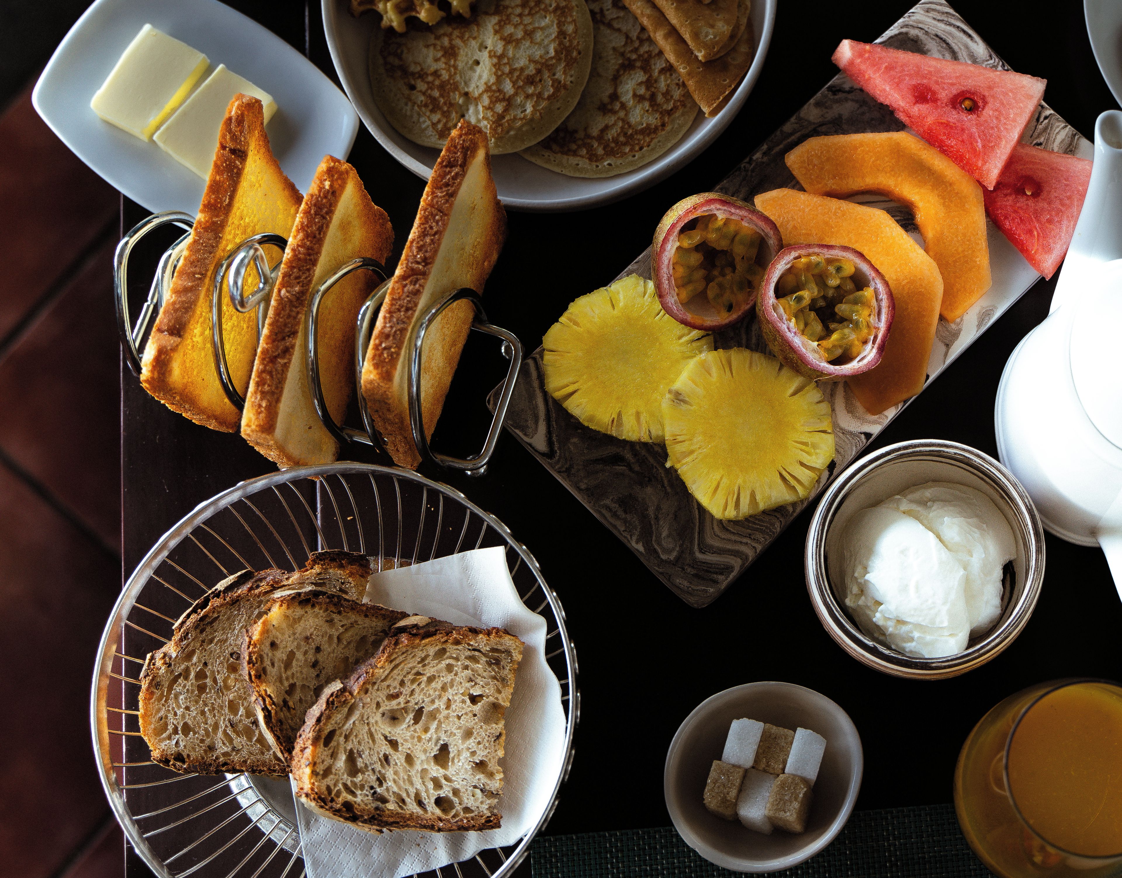 Mesa de café da manhã com torradas, panquecas, frutas e uma xícara de café.