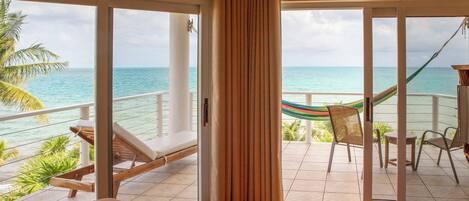 A balcony with a view of the ocean, a hammock, and lounge chairs.