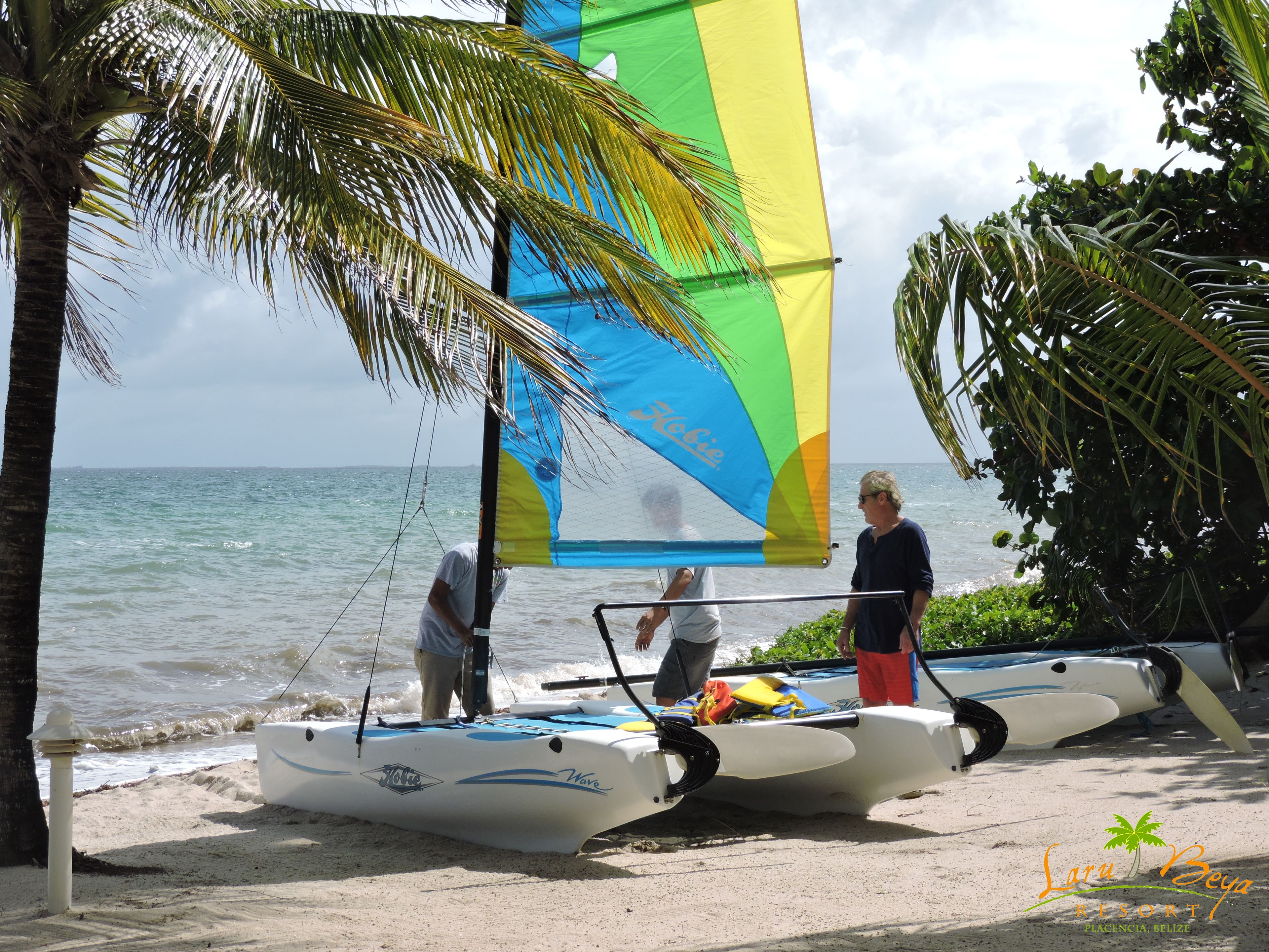 A beach with a sailboat and a person standing on the sand.