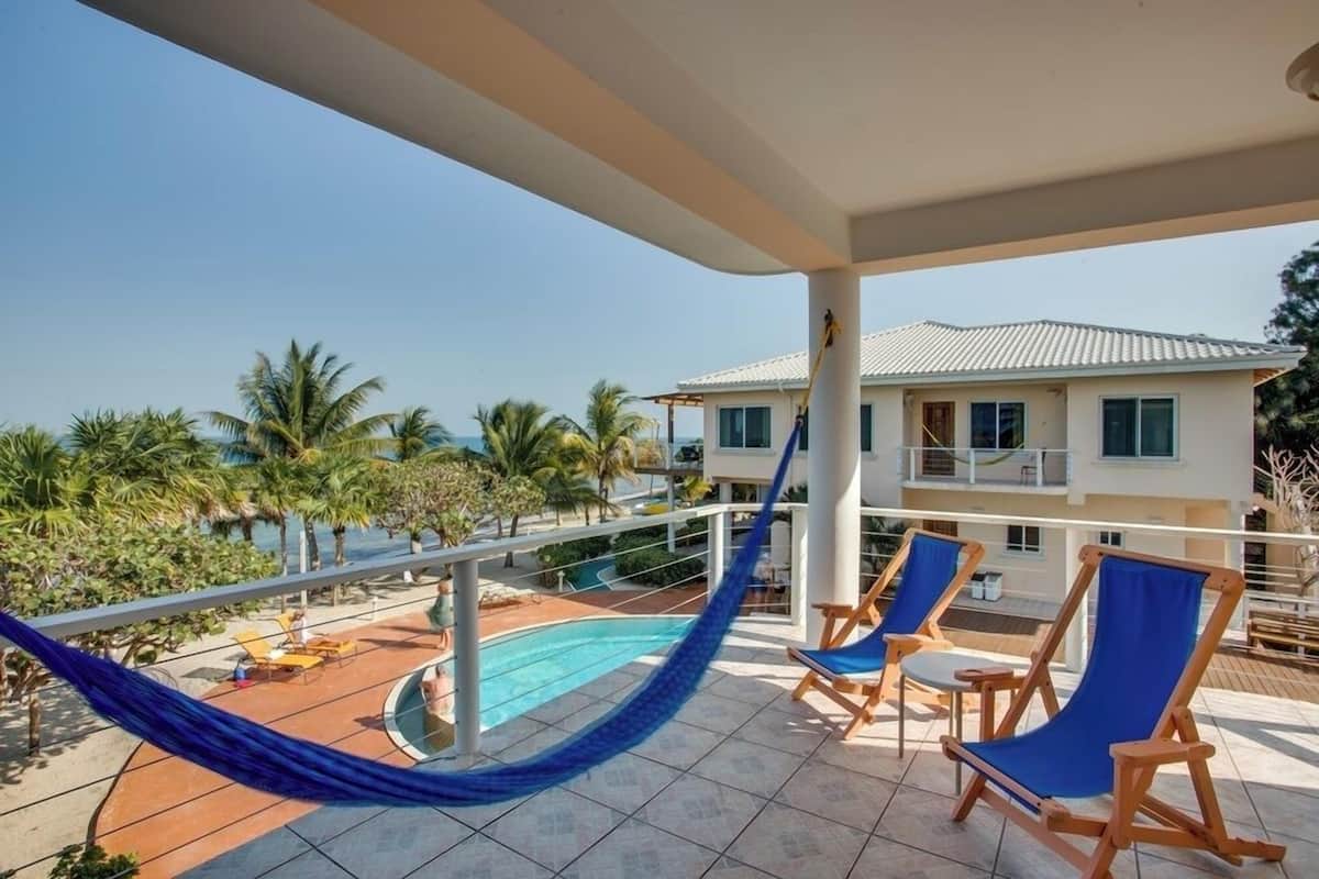 A poolside area with a hammock, lounge chairs, and a view of the ocean and a building.