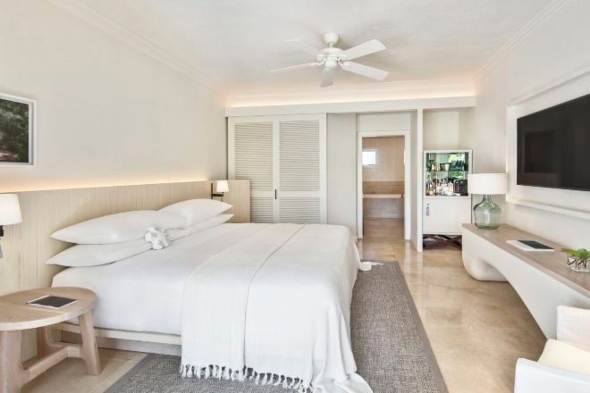 A modern hotel room with a bed, a ceiling fan, a TV, and a small table.
