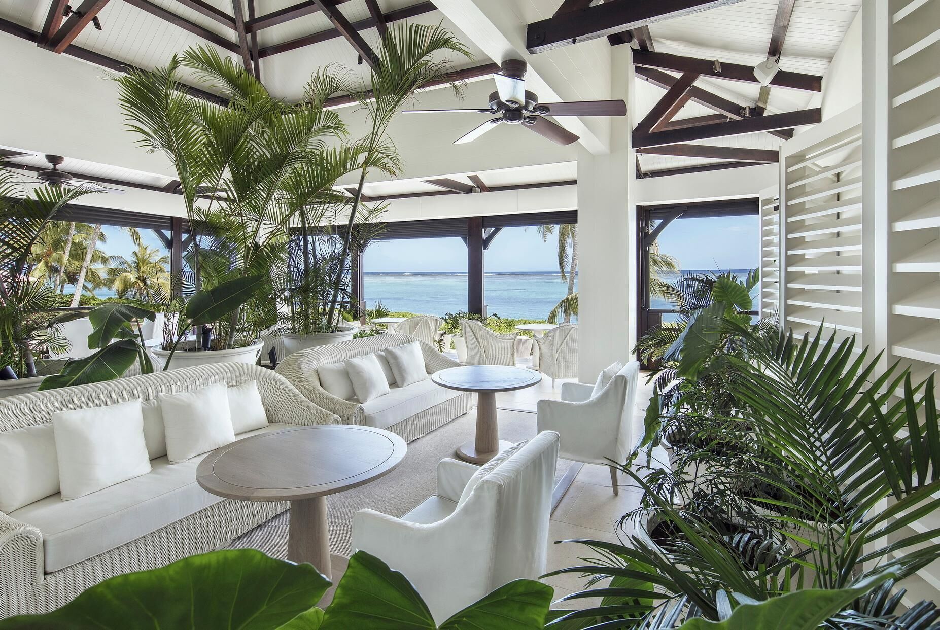 A covered outdoor seating area with white wicker furniture, a ceiling fan, and a view of the ocean.