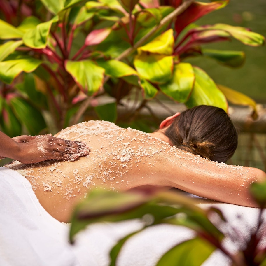A person receiving a massage outdoors with plants in the background.