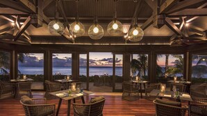 Un restaurante con mobiliario de mimbre y vista al océano.