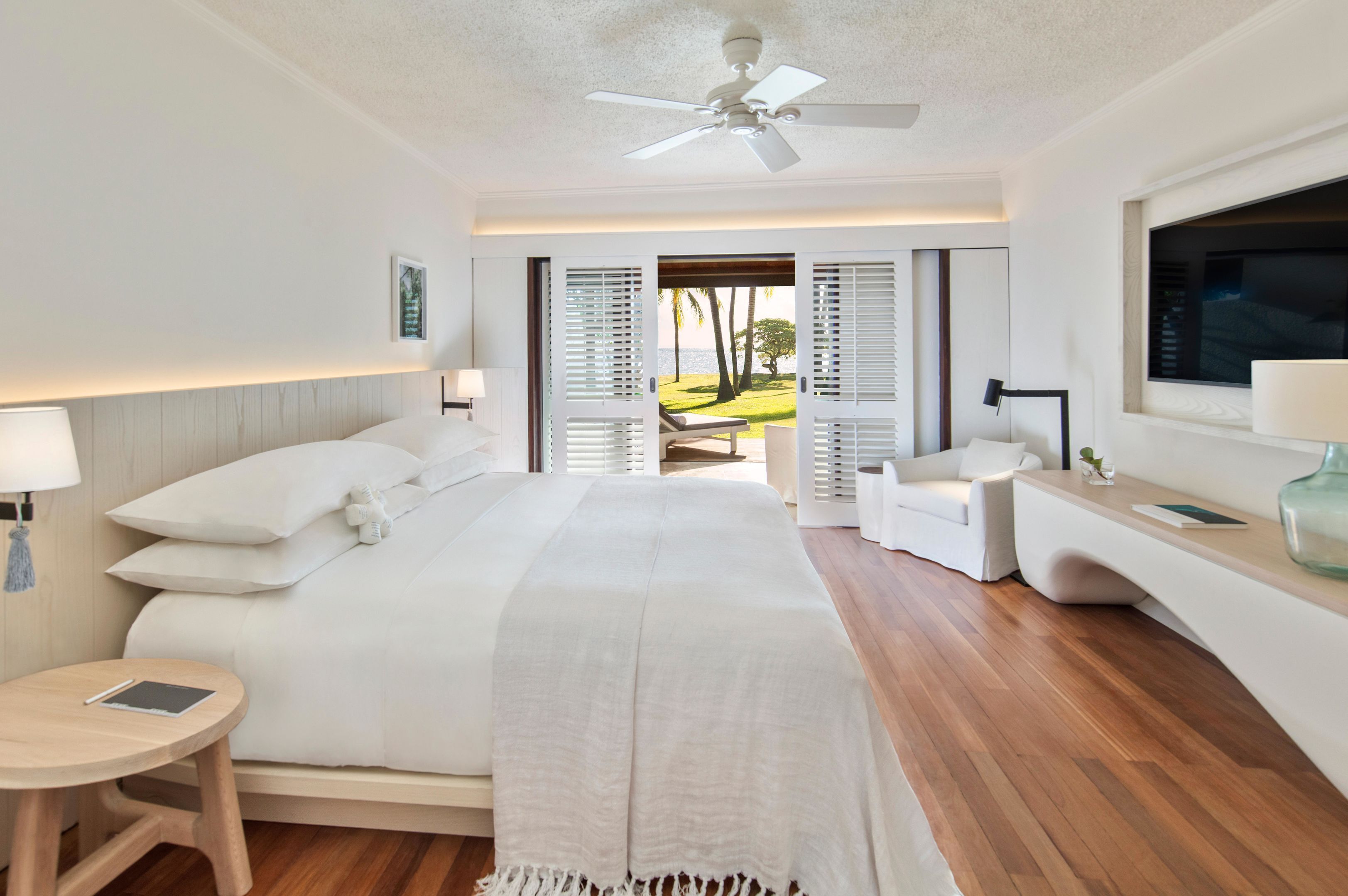 A modern hotel room with a bed, bedside tables, a TV, and a view of the outdoors.