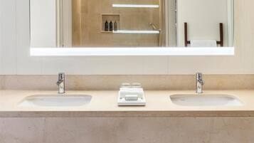 Un baño moderno con dos lavamanos, un espejo grande y un banco de madera con toallas y artículos de aseo.