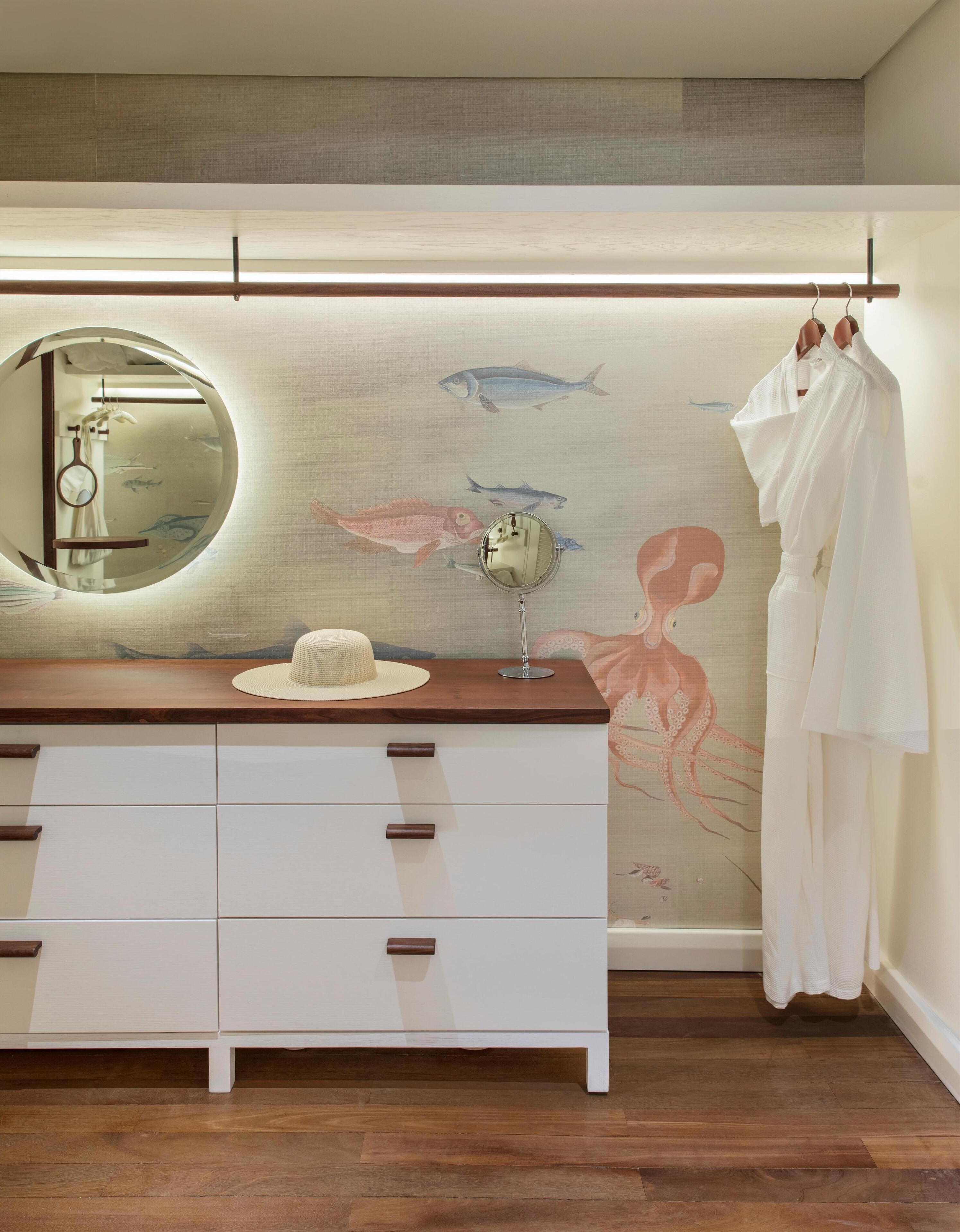 Un baño con tocador de madera, un espejo redondo y un mural en la pared con peces y un pulpo.