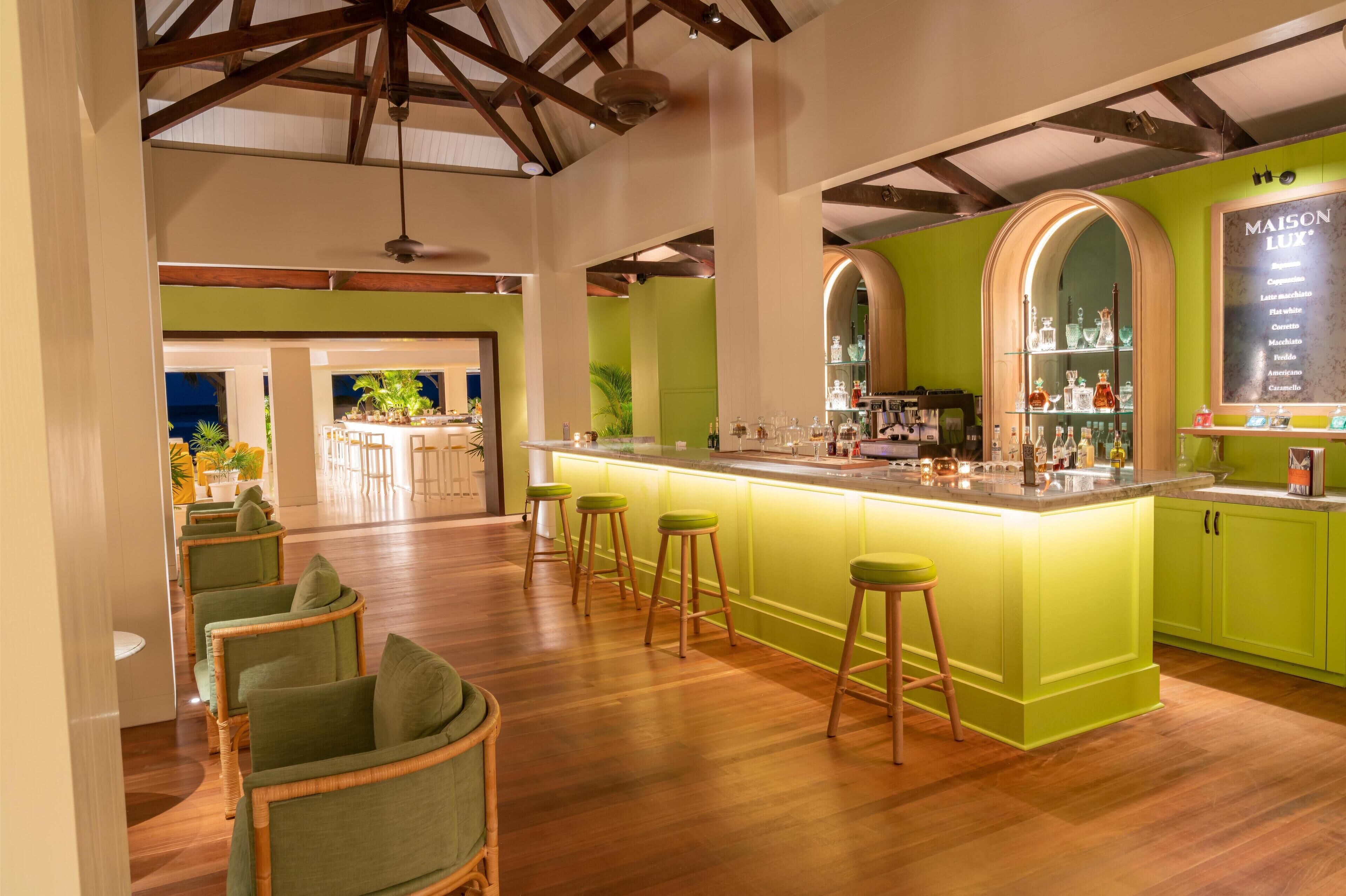 A modern kitchen with a green island, bar stools, and a bar area with glassware.