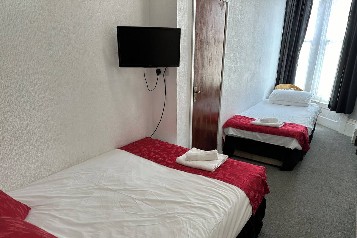 A hotel room with two beds, a TV mounted on the wall, and a window with curtains.