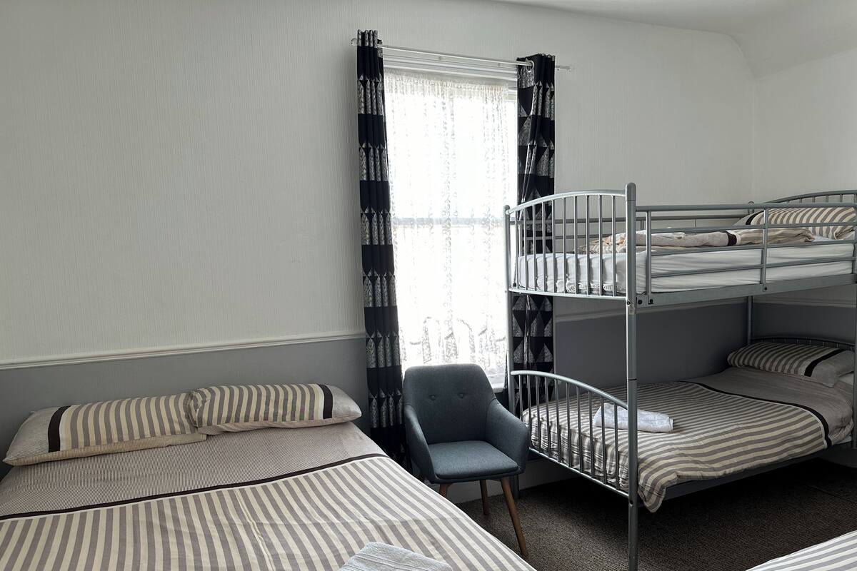 A room with bunk beds, a chair, and a window with patterned curtains.