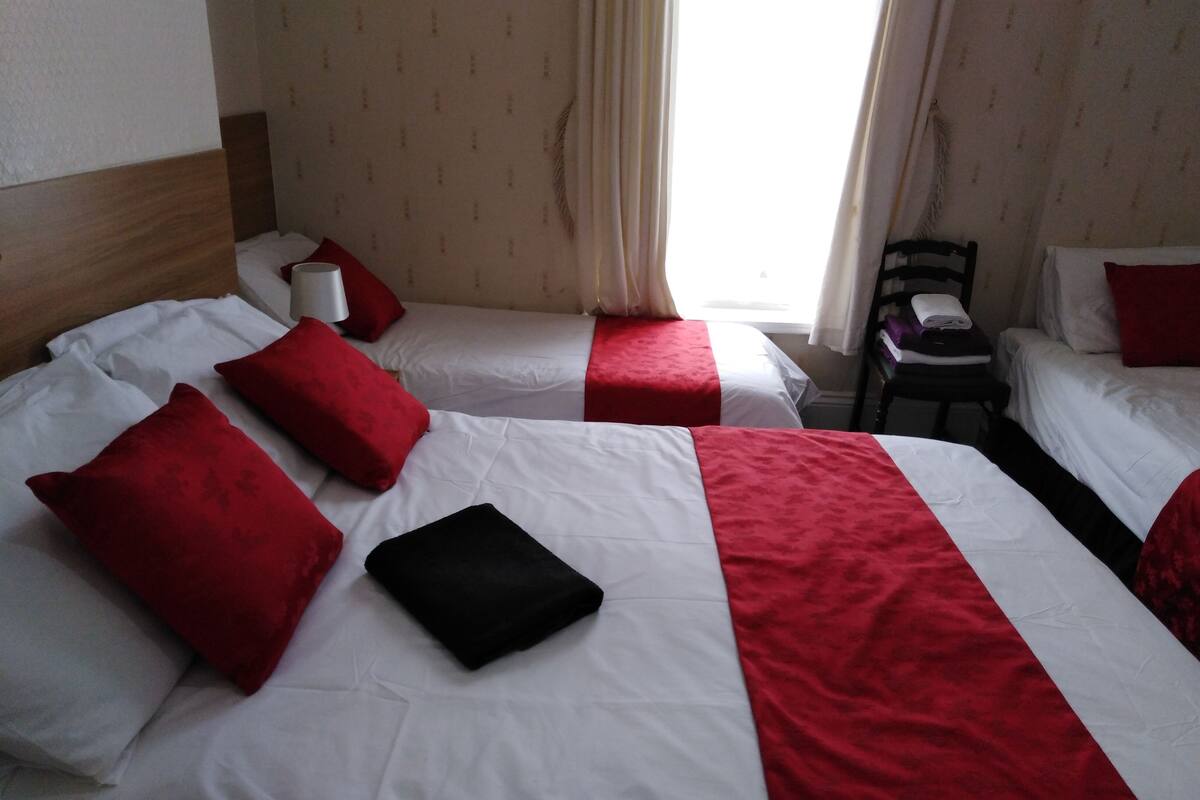 A hotel room with two beds, each with red and white bedding, a wooden headboard, and a chair with a folded towel.