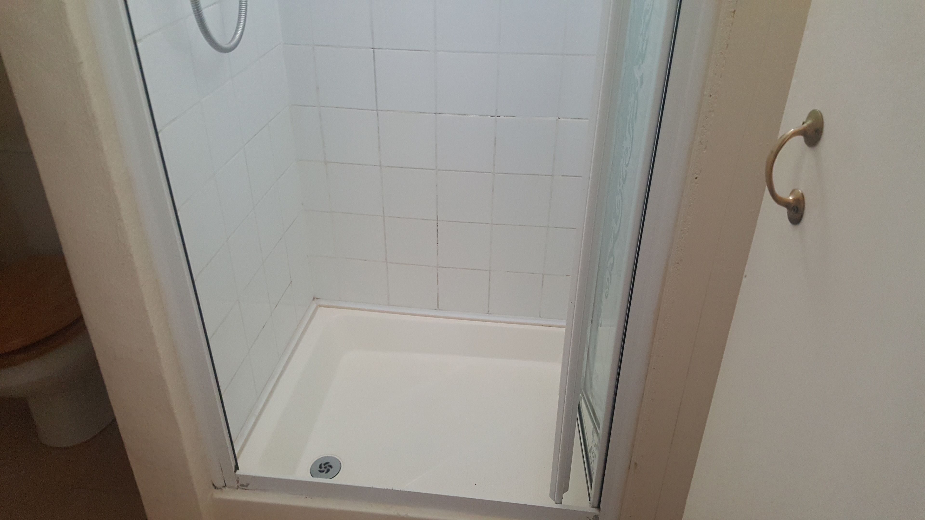 Suihkutila, jonka seinät on laatoitettu valkoisilla laatoilla ja jossa on lasiovi.
