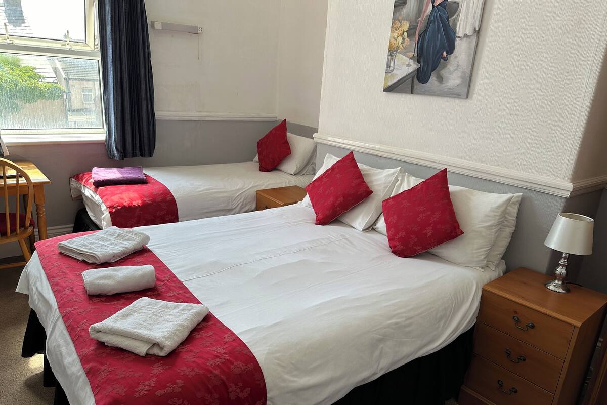 A hotel room with two beds, each with white and red bedding, a wooden nightstand with a lamp, and a painting on the wall.