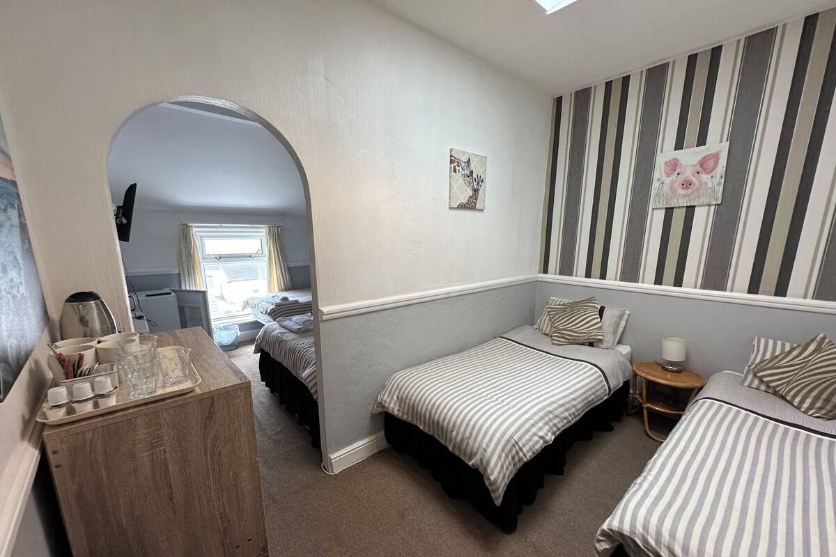A bedroom with two single beds, a wooden dresser, a small table with a lamp, and a painting on the wall.