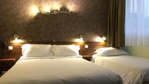 A hotel room with a large bed, two bedside tables, a wall-mounted light fixture, and a window with curtains. - Hotel Saint Aignan (Orléans)