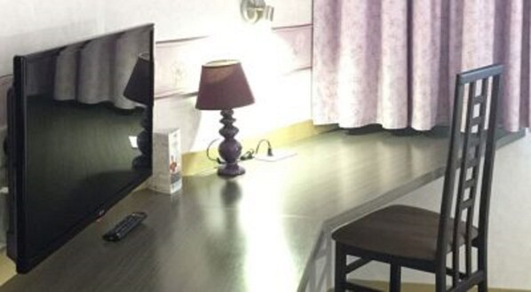 A room with a TV, a lamp, a chair, and a remote control on a wooden table. - Hotel Saint Aignan (Orléans)