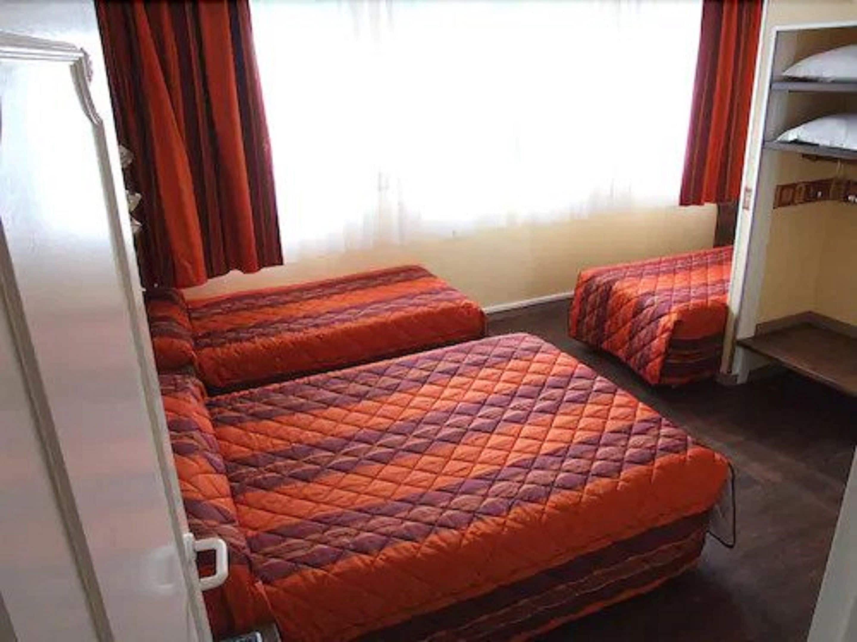 Quarto compacto com duas camas, um guarda-roupa e uma janela com cortinas.