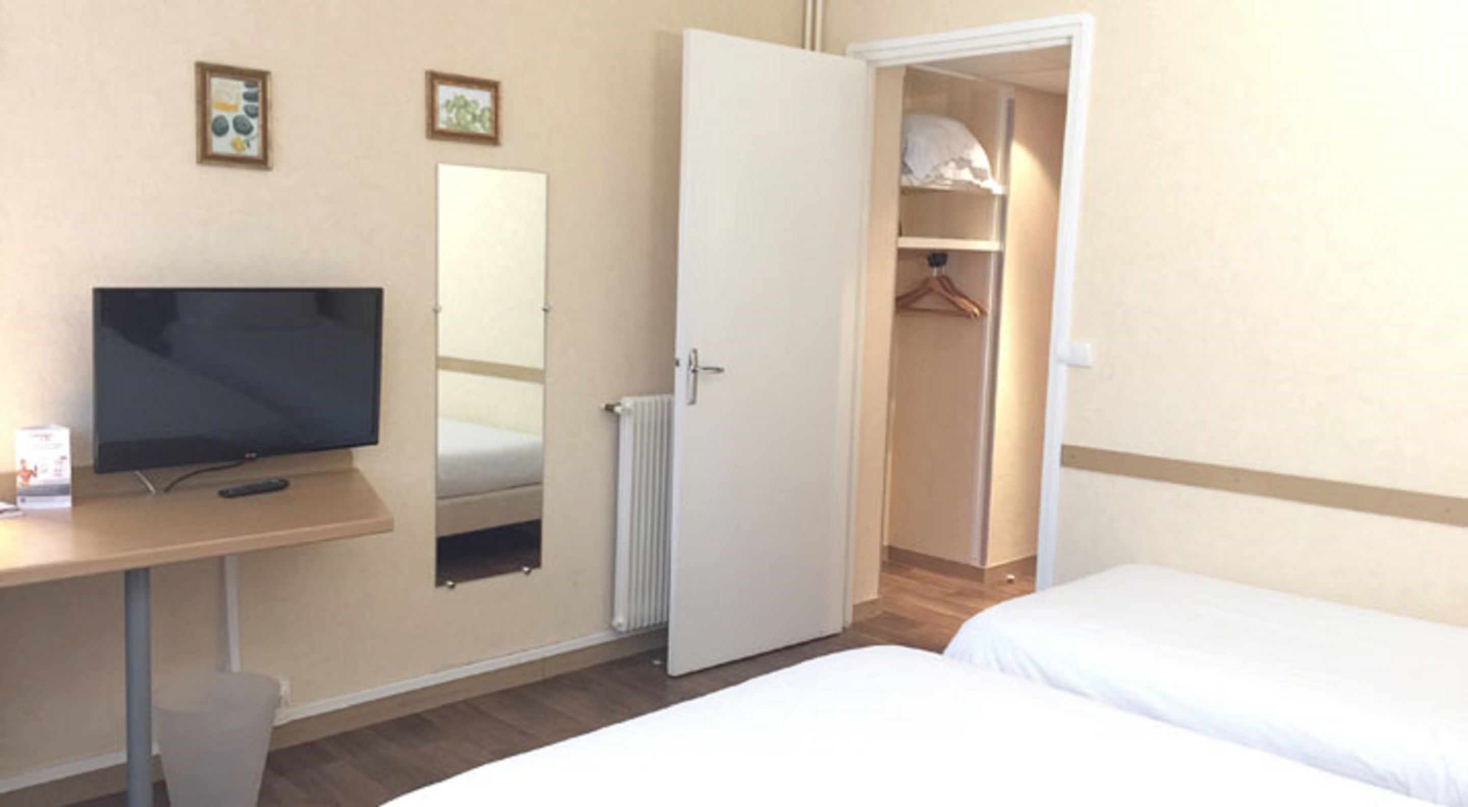 Una habitación de hotel con cama, televisión, escritorio, espejo y armario.