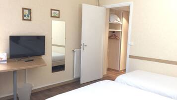 Una habitación de hotel con cama, televisión, escritorio, espejo y armario.