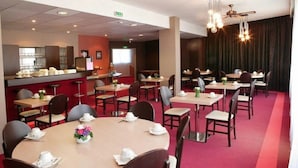 A hotel dining area with round tables, chairs, and a bar counter. - Hotel Saint Aignan (Orléans)