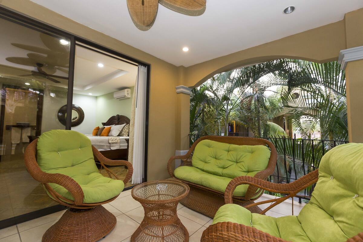 A balcony with wicker furniture and a view of palm trees.