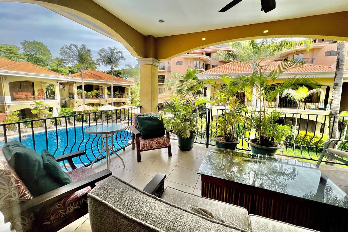 A balcony with a pool, potted plants, and a table with chairs.