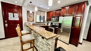 A kitchen with a granite countertop, a built-in island, wooden cabinets, stainless steel appliances, and a tiled floor. - Monte Carlo Luxury Condominiums (Jacó)