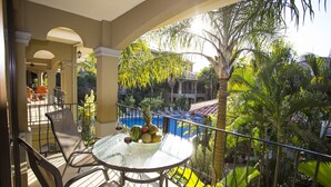 A balcony with a glass table and chairs, overlooking a swimming pool and lush greenery. - Monte Carlo Luxury Condominiums (Jacó)