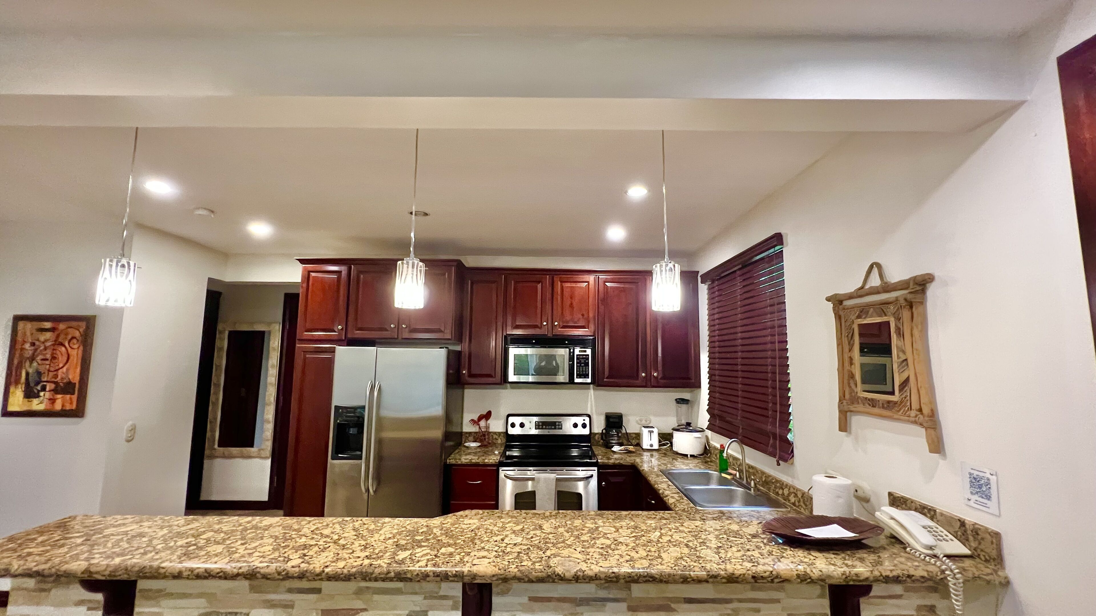 A kitchen with granite countertops, stainless steel appliances, wooden cabinets, and pendant lighting.