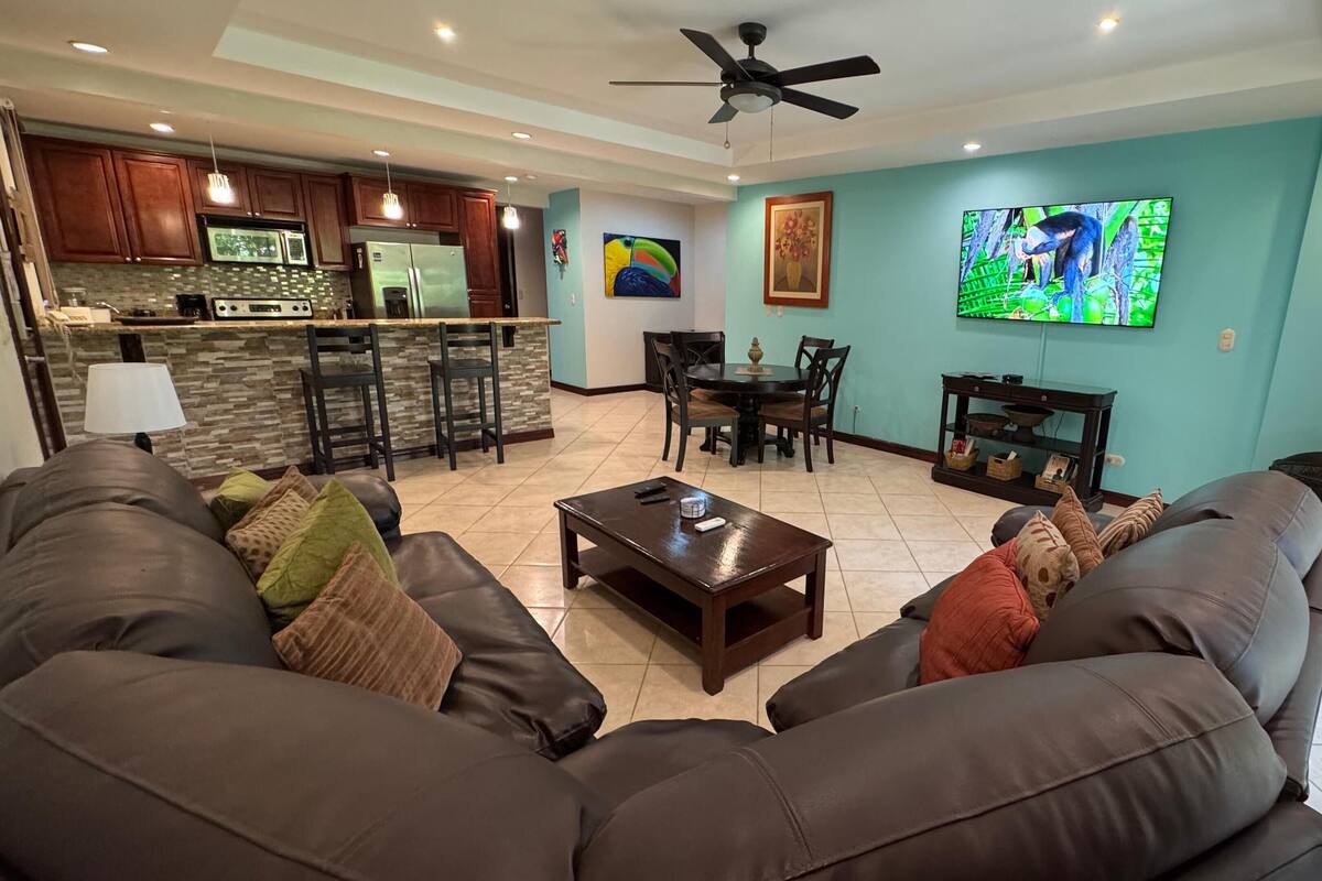 A modern living room with a large leather sofa, a coffee table, and a TV mounted on the wall.