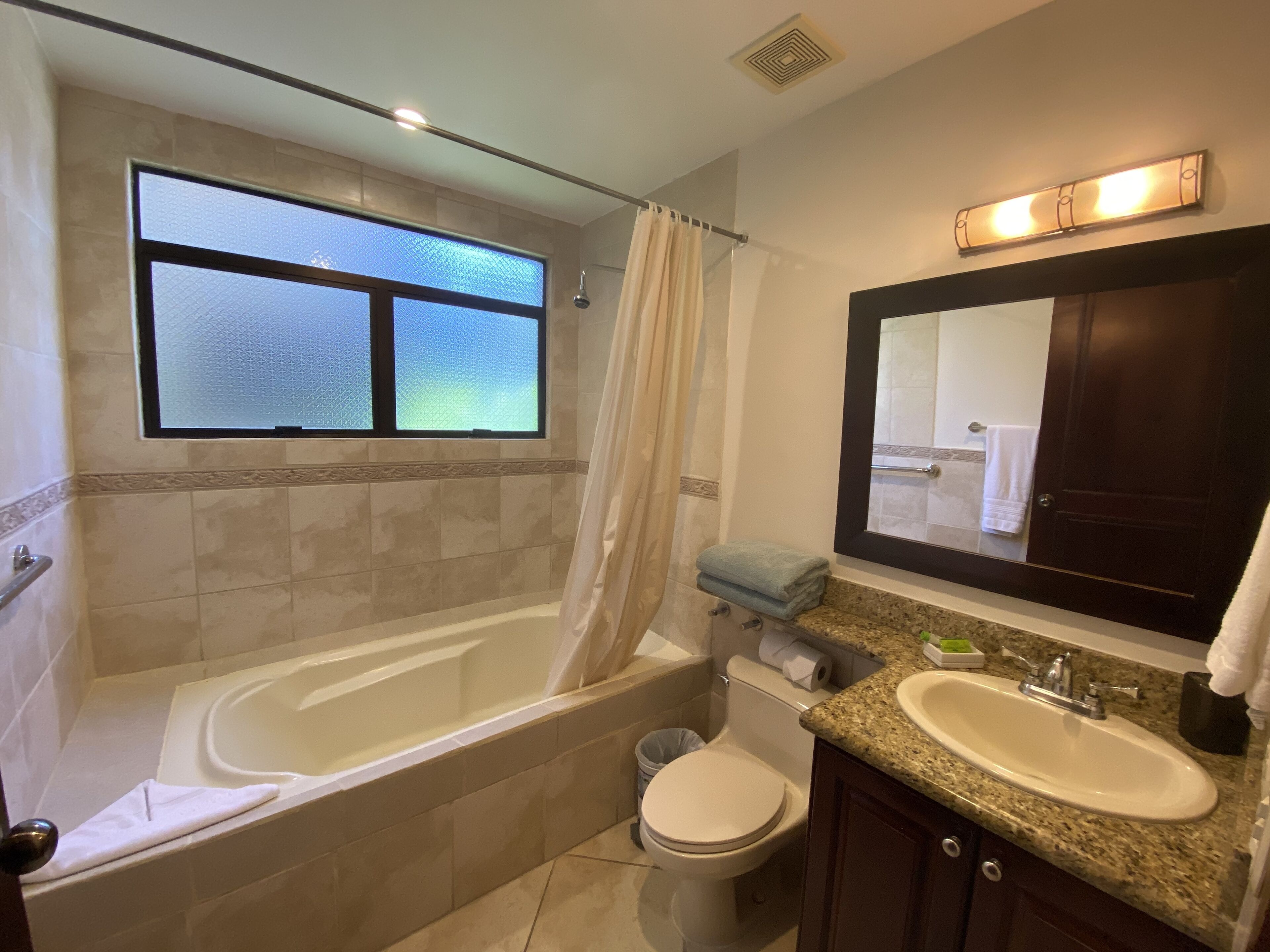 A bathroom with a bathtub, toilet, sink, and a window with frosted glass.
