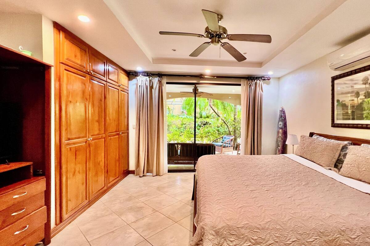 A bedroom with a bed, a ceiling fan, a wardrobe, and a balcony with curtains.