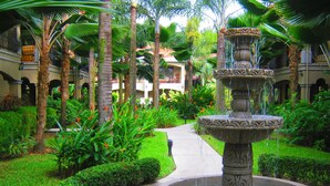 A courtyard with a central fountain, surrounded by lush greenery and palm trees. - Monte Carlo Luxury Condominiums (Jacó)