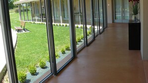 A corridor with large glass doors leading to a covered outdoor area with a bench and small plants.