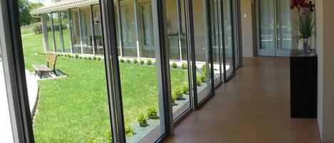 Un pasillo con grandes puertas de cristal que dan a un área exterior cubierta, con un banco y plantas pequeñas.
