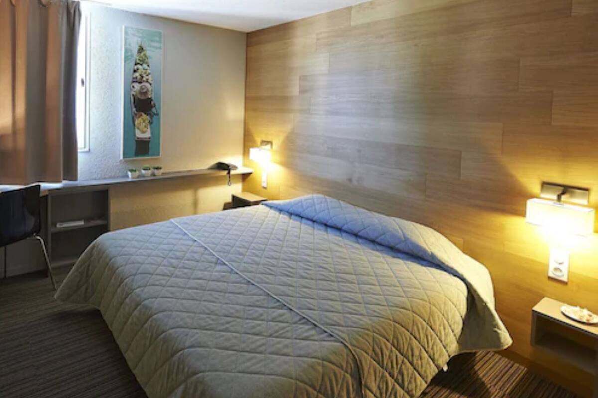 A hotel room with a large bed, a desk, and two bedside lamps.