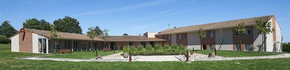 A modern building with a curved roof and brick facade, featuring a central courtyard with benches and greenery.